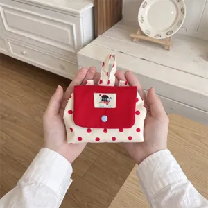 Gros plan d'une mini pochette de rangement à pois rouges tenue par les mains pour accessoires.