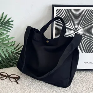 Bolso tote de lona negra con correa ancha en una escena minimalista con accesorios.