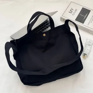 Bolso tote grande de lona negra con correa ancha mostrado con un portátil para escala