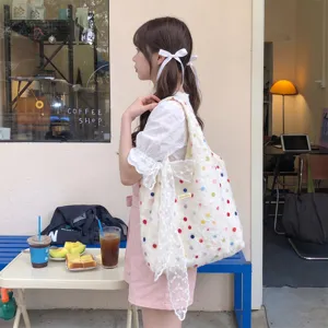 Seitenansicht einer großen weißen Canvas-Tasche mit bunten Punkten und Spitzen-Schleife