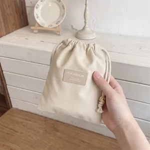 Detailopname van een minimalistisch beige opbergzakje met trekkoord en een FHUASHIJIE-patch.