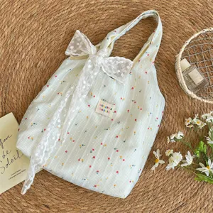 Vista detallada de un bolso tote floral a rayas con un lazo de encaje blanco sobre paja