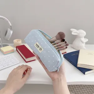 Dettaglio di un astuccio azzurro a pois in tessuto usato come porta pennelli da trucco su una scrivania.