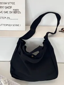 Bolso tote de lona negra con correa ancha para el hombro en un entorno minimalista