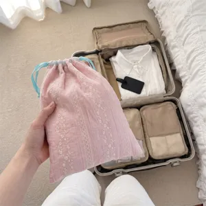 Pink floral embroidered drawstring pouch for travel storage held against suitcase