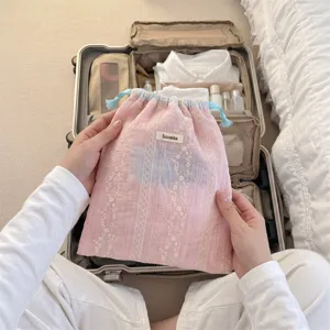 Detailed view of pink floral embroidery drawstring bag held over a travel suitcase