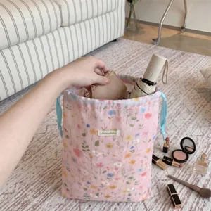 Detailed view of a pink floral drawstring bag being filled with travel items and makeup