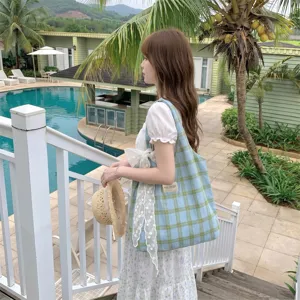 Borsa tote in tela a quadretti azzurri indossata da una modella vicino a una piscina
