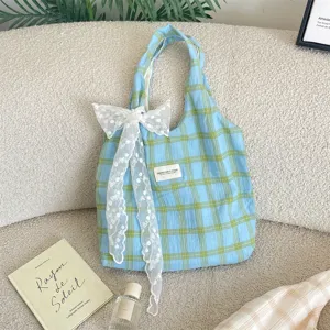 Borsa tote a scacchi azzurro chiaro con grande fiocco di pizzo bianco su divano beige