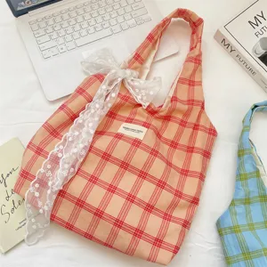 Dettaglio di una borsa shopping a quadri pesca con elegante fiocco in pizzo bianco su scrivania