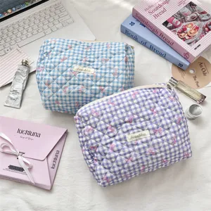 Detailed view of quilted plaid toiletry bags with pink bows and lifestyle props
