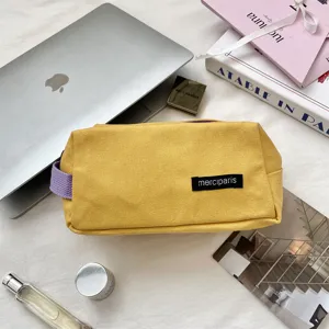 Close-up van een gele canvas etui met een paarse draagriem en een zwart merklabel