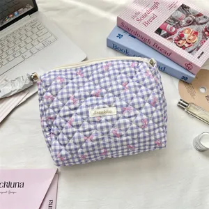 Macro view of a purple quilted plaid cosmetic bag featuring pink bows and a Surakku label