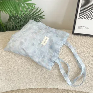 Detailed view of light blue tie-dye floral tote bag on a cozy white textured surface
