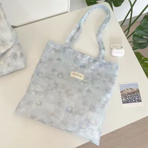Detailed view of ice blue tie-dye floral tote bag with a woven brand label on white table