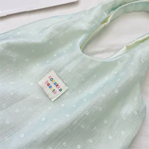 Detailopname van een lichtblauwe bloemen gaas tas met kleurrijk 'sozakka' merklabel