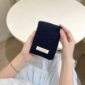 Dettaglio di un porta passaporto in lana blu scuro con pois bianchi ed etichetta ricamata.