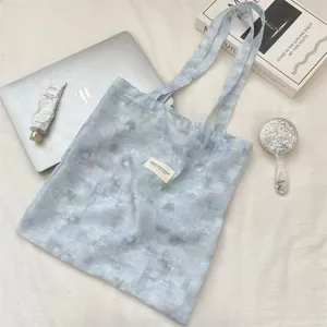 Close-up of a light blue tie-dye floral tote bag with a woven brand label detail