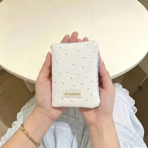 Primo piano di un porta passaporto bianco a pois con bordi a scacchi blu ed etichetta.