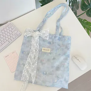 Macro detail of a blue tie-dye floral tote bag with a charming white lace bow accessory.