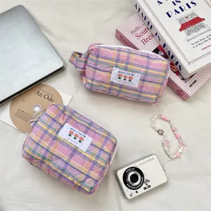Close-up of pastel plaid quilted cosmetic bags on a desk with lifestyle travel props