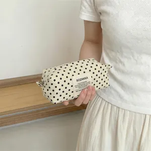 Close-up of off-white canvas cosmetic pouch with black polka dots held in hand for detail