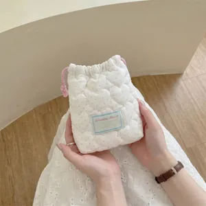 Detalle de una bolsa acolchada crema con forma de corazón, lunares y cordón rosa