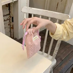 Detail shot of a delicate pink lace drawstring storage pouch held by hand in a cozy cafe.