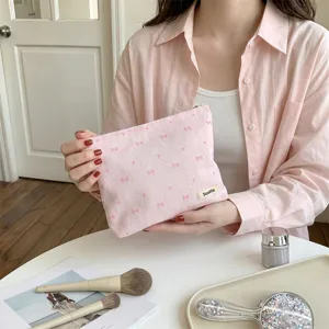 Detailed view of pink makeup bag featuring delicate heart and bow embroidery texture.