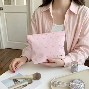 Detailed view of a pink bow heart embroidered cosmetic bag held in a soft lifestyle setting