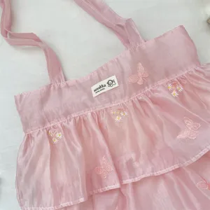 Detalle de bolso tote de organza rosa con capas de volantes y bordado de mariposas.