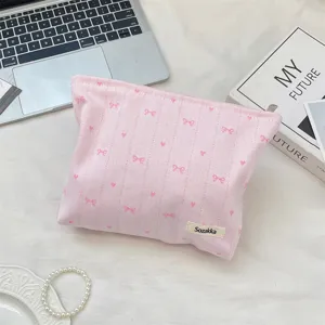 Pink striped makeup bag with bow embroidery shown in a lifestyle daily desk setting