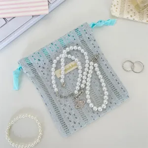 Close-up of a light blue hollow lace drawstring pouch with pearl jewelry accessories