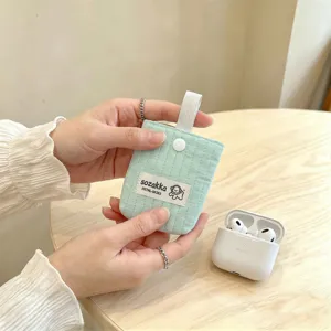 Close-up of a mint green quilted fabric earphone pouch being held by hand on a table