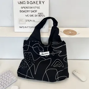Minimalistische schwarze Canvas-Tasche mit weißen abstrakten Mustern auf einem Schreibtisch.