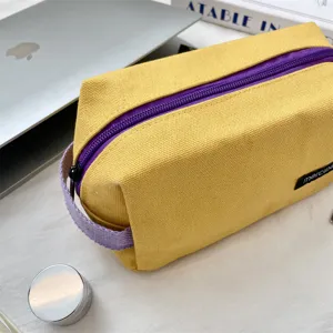 Detail van een gele canvas etui met een paarse ritssluiting en een handig handvat.