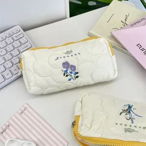 Detalle del bordado floral y textura acolchada en un estuche de lápices blanco crema