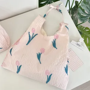 Gros plan d'un sac cabas plissé rose avec des tulipes brodées et des lanières à cordon