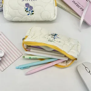 Vista detallada del estuche acolchado crema con bordado de flores y bolígrafos