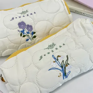 Primer plano de estuches acolchados con delicados bordados florales y cremalleras amarillas.