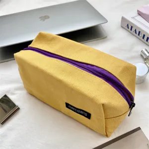 Detailopname van een minimalistische gele canvas etui met een paarse ritssluiting.