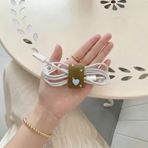 Dettaglio macro dell'organizzatore per cavi verde con un bottone a forma di cuore.