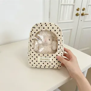 Detail view of a polka dot doll storage bag with a transparent window showing a plush toy
