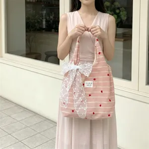 Lovely pink striped tote bag with heart embroidery and lace bow held by a model.