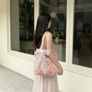 Detailed view of pink striped tote bag featuring heart embroidery and lace bow