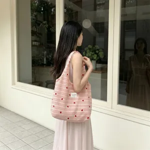Detailed shot of a pink and white striped tote bag with heart embroidery on a model