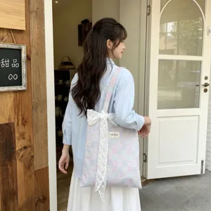 Detail view of a pink and blue plaid canvas tote bag featuring a white lace bow accent