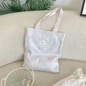 Detail view of a pink and blue checkered canvas tote bag with a brand label on a soft surface.