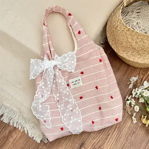 Close-up of pink striped tote bag with heart embroidery and lace bow detail.