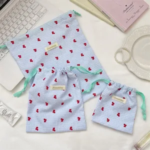 Vista detallada de tres bolsas de cuadros azules con bordado de cerezas rojas y cordón.